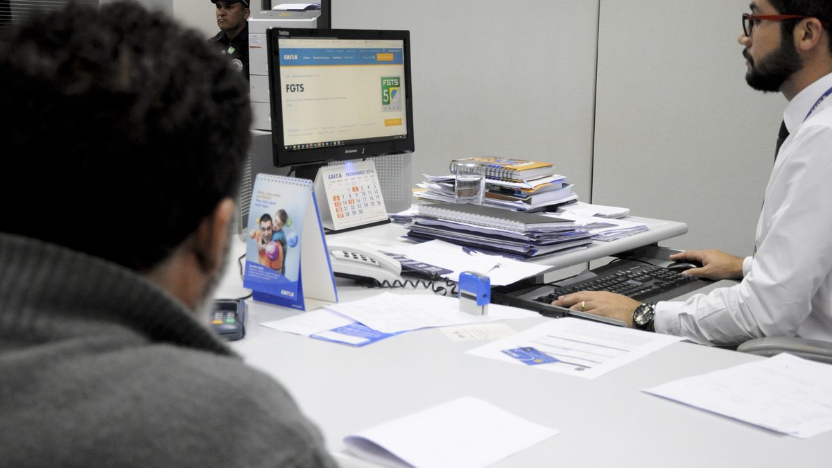 Cliente é atendido no guichê de uma agência da Caixa Econômica Federal, com a tela do sistema do FGTS no computador, em Brasília