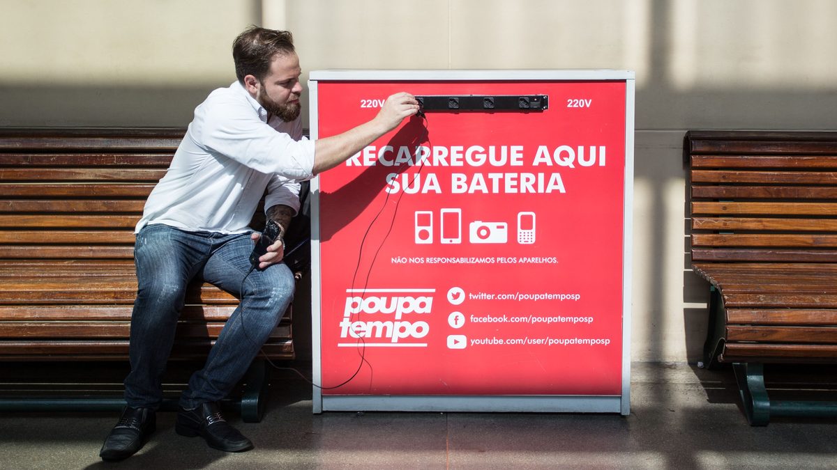 Homem carrega o celular num totem de recarga de bateria em uma unidade do Poupatempo, em São Paulo