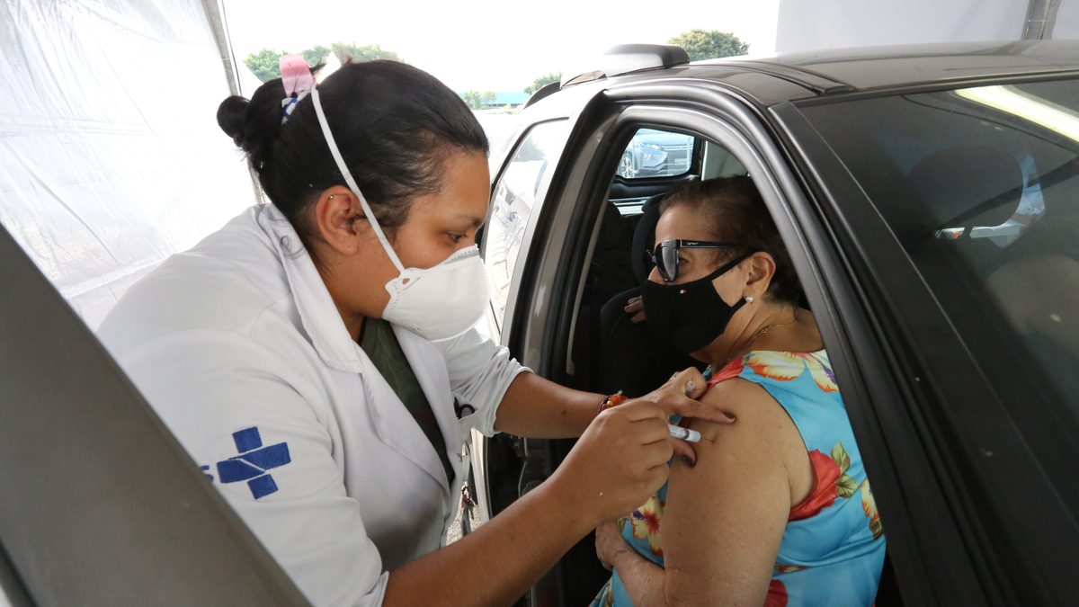 Profissional de saúde vacina uma idosa dentro do carro num posto de vacinação em São Paulo, em março de 2021