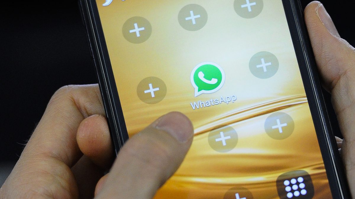 Mãos seguram um celular com o ícone do WhatsApp na tela